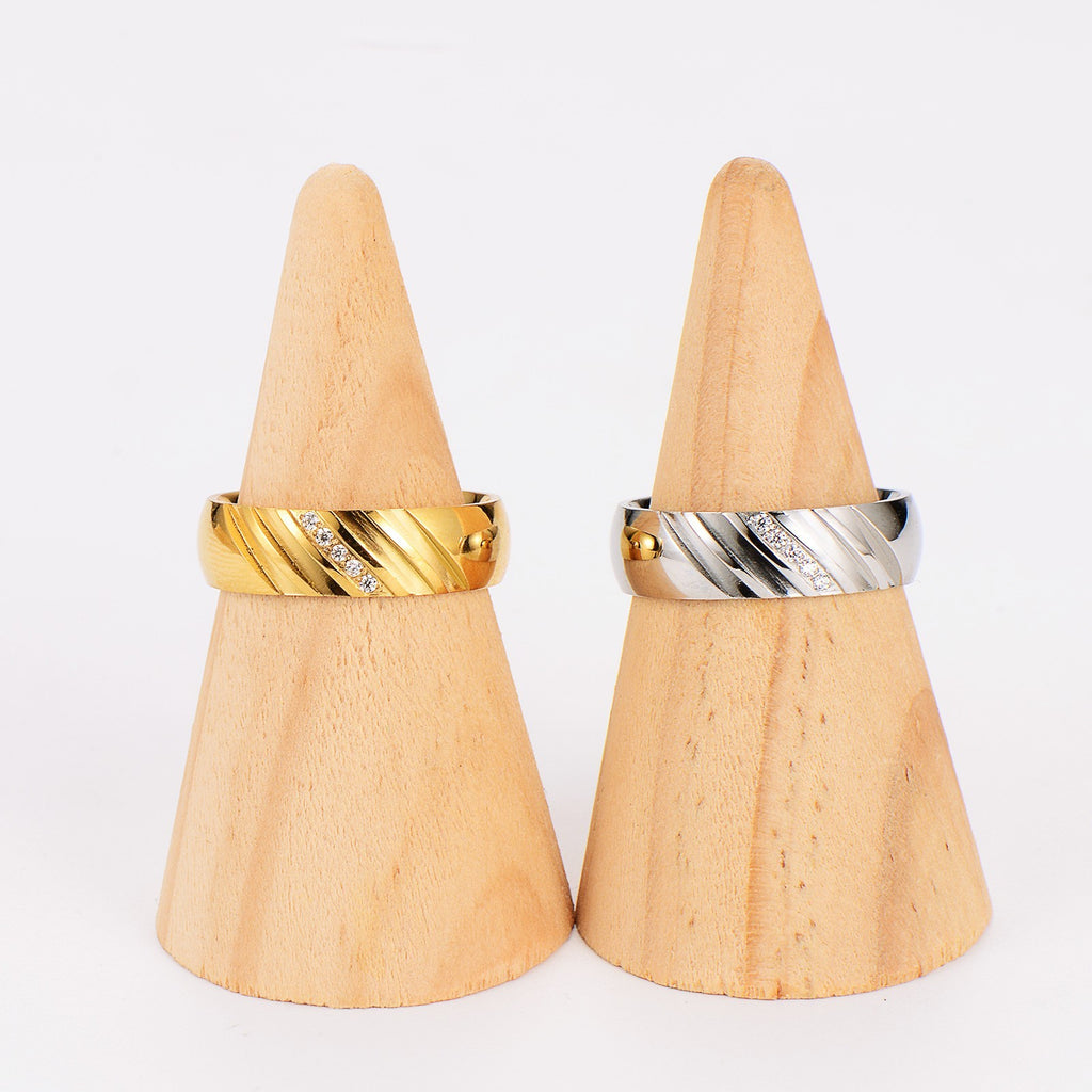 Zwei breite Ringe aus Gold und Silber mit Zirkonia, auf Holzständern präsentiert.