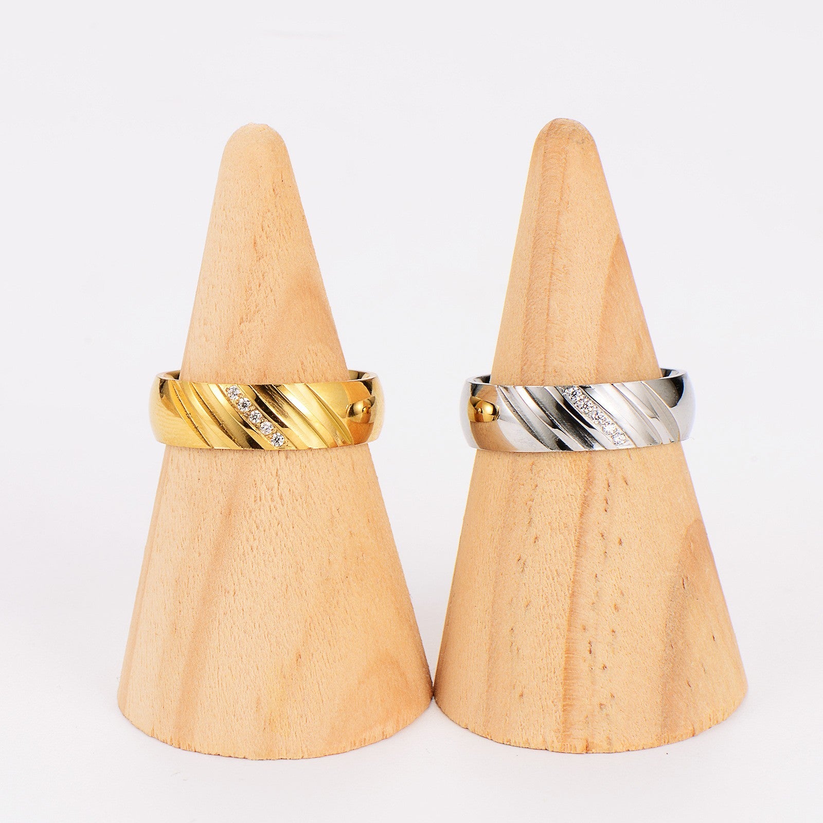 Zwei breite Ringe aus Gold und Silber mit Zirkonia, auf Holzständern präsentiert.