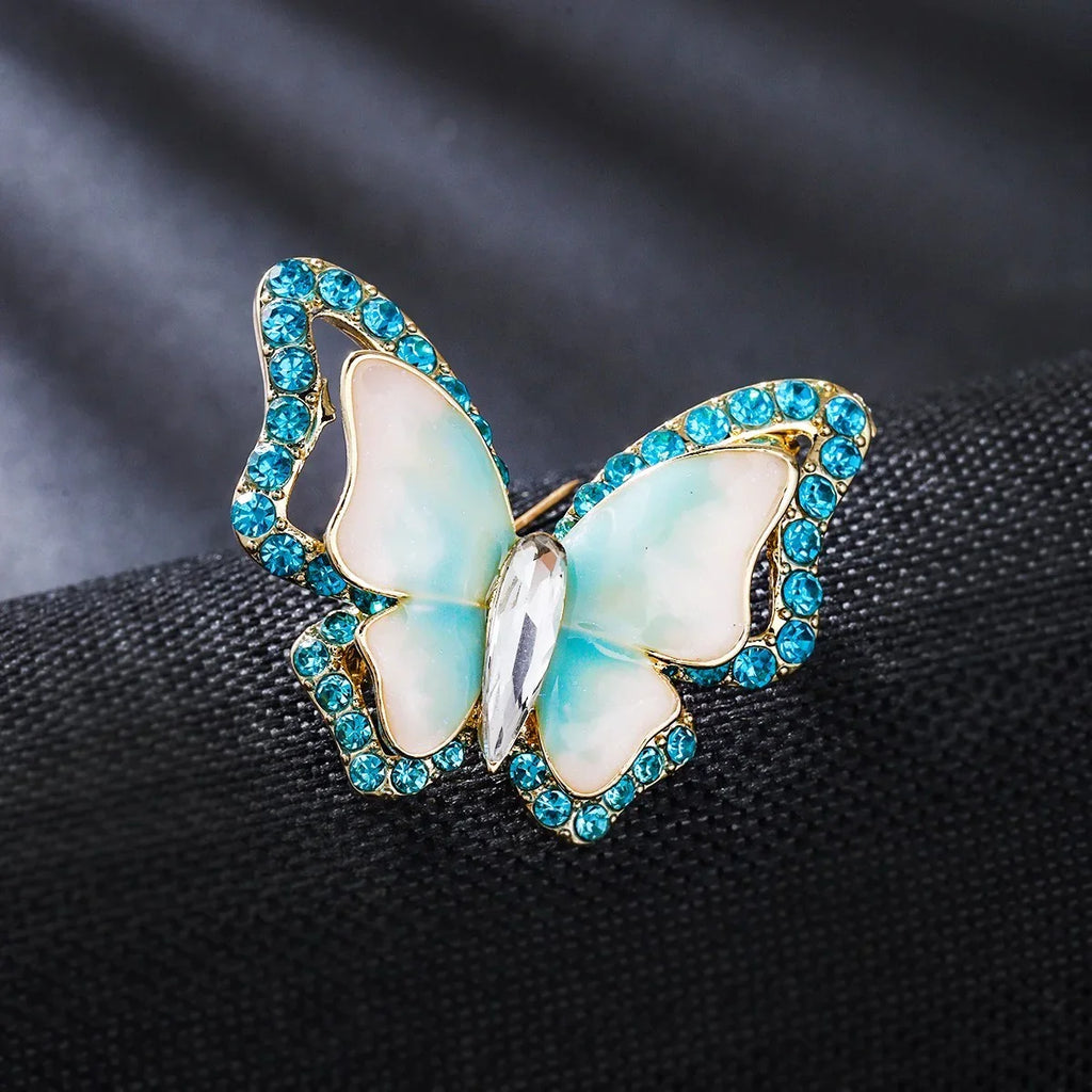 Schmetterling Ring mit blauen Zirkonia und goldener Fassung auf dunklem Stoff